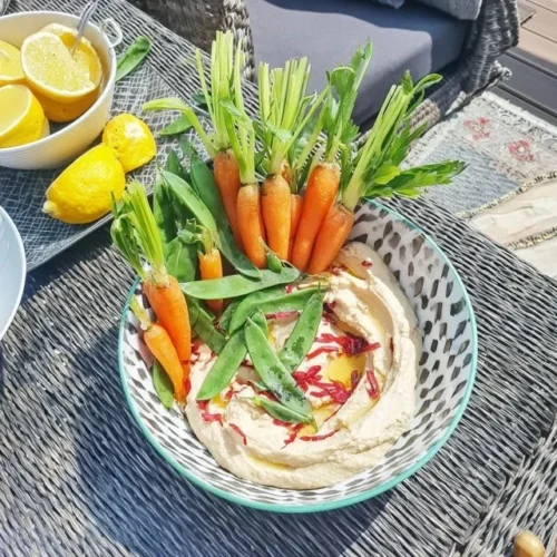 Piatto aperitivo con hummus, carote nuove e piselli mangiatutto.